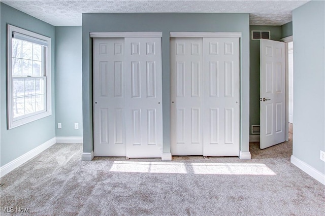 unfurnished bedroom featuring multiple closets, a textured ceiling, and light colored carpet