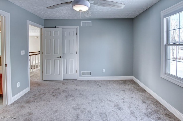 carpeted empty room with a textured ceiling, ceiling fan, and plenty of natural light