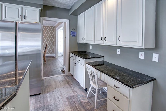 kitchen with stainless steel refrigerator, white cabinets, dark stone countertops, and light hardwood / wood-style flooring