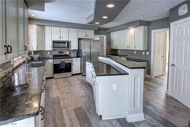 kitchen with a textured ceiling, a kitchen island, white cabinetry, appliances with stainless steel finishes, and sink