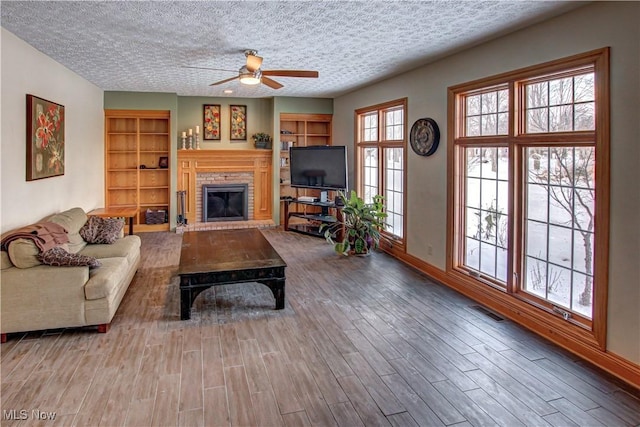 living room with a textured ceiling, built in features, ceiling fan, and plenty of natural light