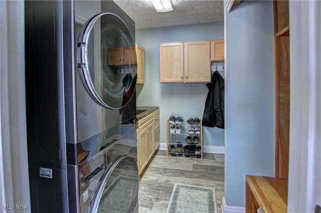 washroom with stacked washer / drying machine, a textured ceiling, cabinets, and light hardwood / wood-style flooring