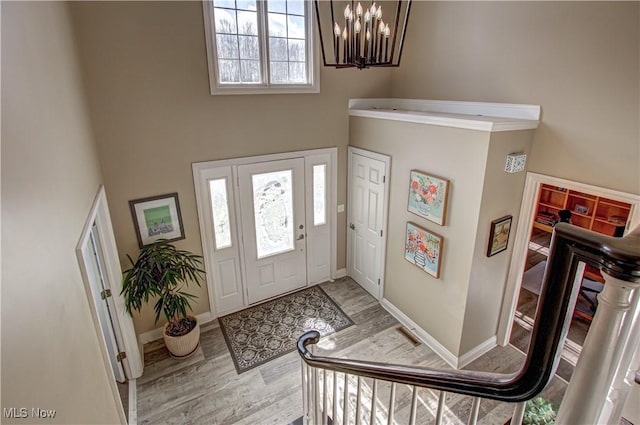 entrance foyer with a towering ceiling, light hardwood / wood-style floors, a healthy amount of sunlight, and a notable chandelier