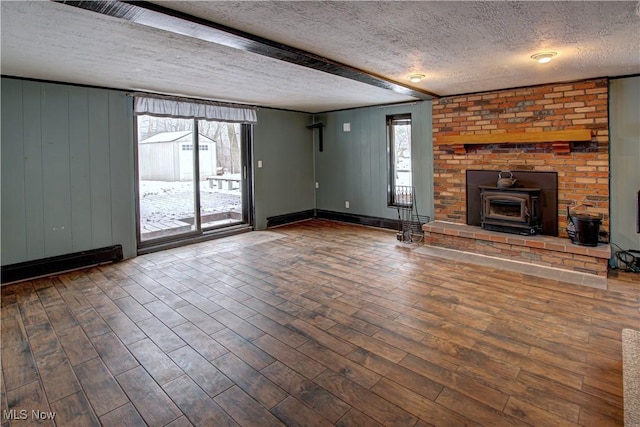 unfurnished living room with wooden walls, a wood stove, hardwood / wood-style flooring, beam ceiling, and a textured ceiling