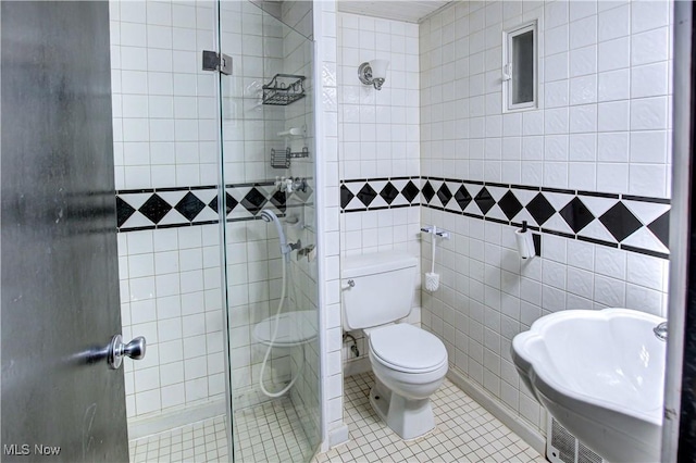 bathroom with tile patterned floors, toilet, a shower with shower door, sink, and tile walls