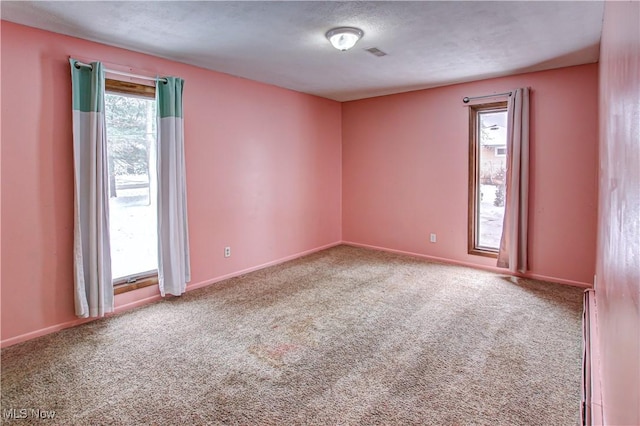 carpeted empty room with a wealth of natural light, a textured ceiling, and baseboard heating