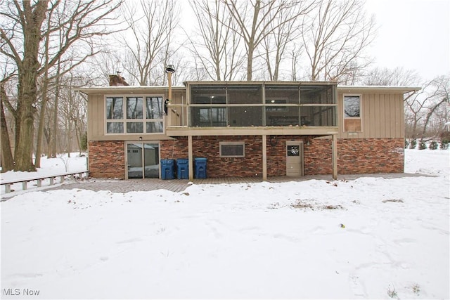 snow covered rear of property with a sunroom