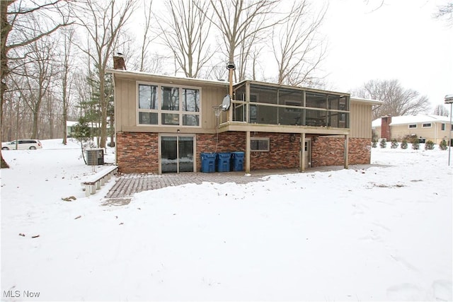 snow covered property with a sunroom and central AC