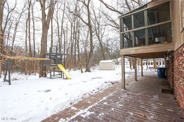 yard layered in snow with a wooden deck, a storage shed, a playground, and a sunroom