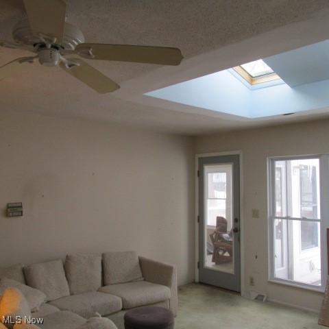 carpeted living room featuring ceiling fan, a skylight, and plenty of natural light