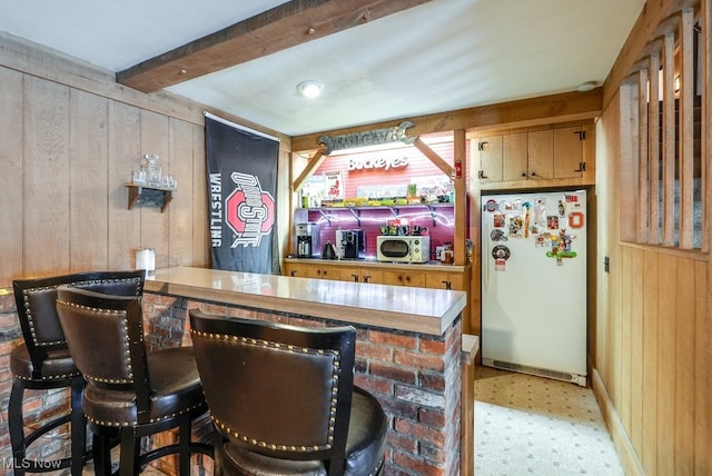 bar with white refrigerator, wood walls, and beamed ceiling