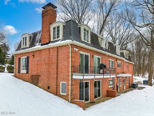 snow covered back of property featuring a balcony and cooling unit