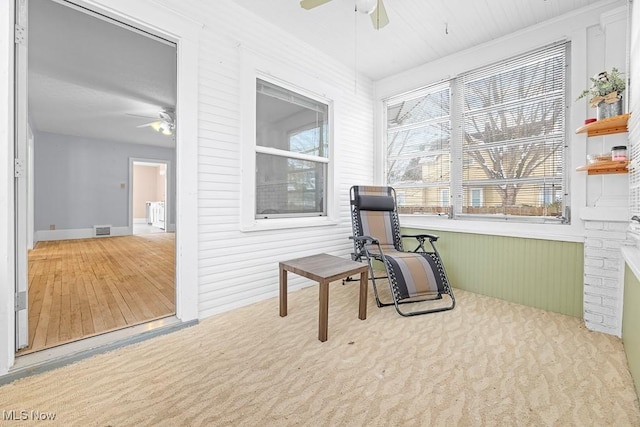 living area featuring ceiling fan, carpet floors, and wood walls