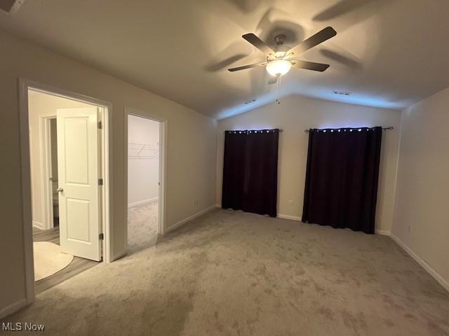 unfurnished bedroom with a closet, lofted ceiling, a walk in closet, ceiling fan, and light carpet