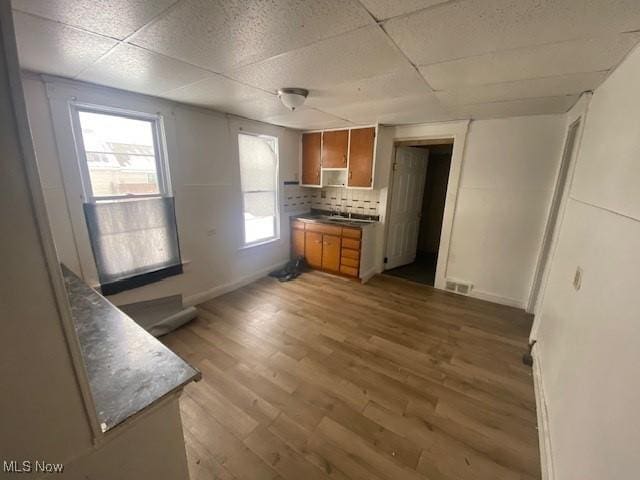 kitchen with a drop ceiling, wood finished floors, visible vents, brown cabinets, and decorative backsplash