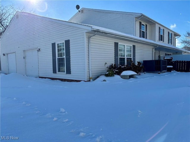 snow covered house with central AC unit and a garage