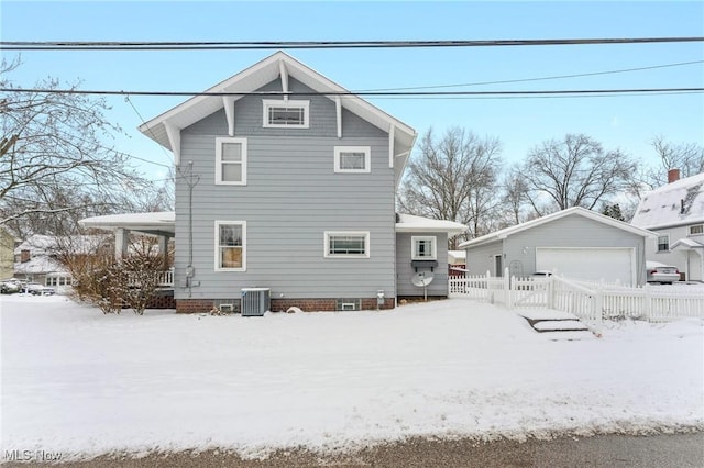 snow covered rear of property featuring central AC, an outbuilding, and a garage