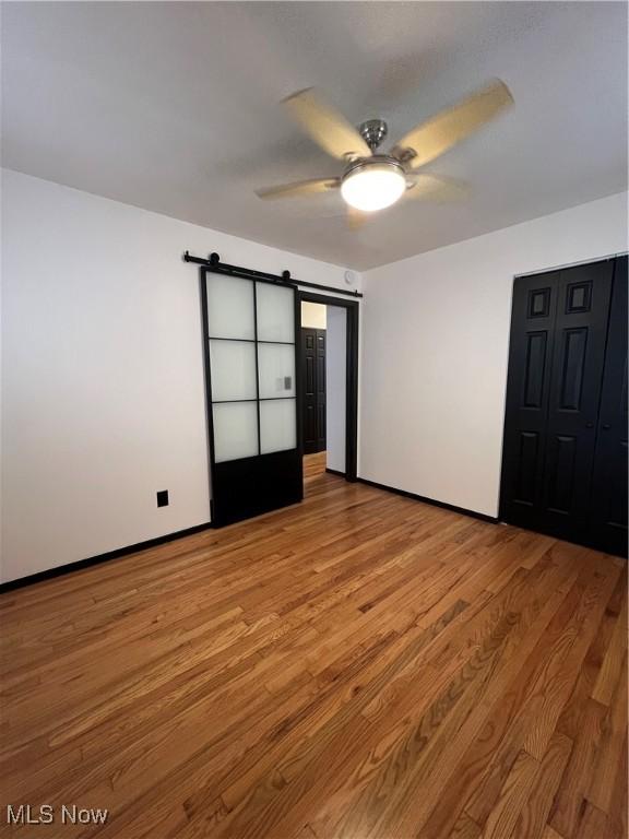 unfurnished bedroom featuring ceiling fan, a barn door, and light hardwood / wood-style flooring