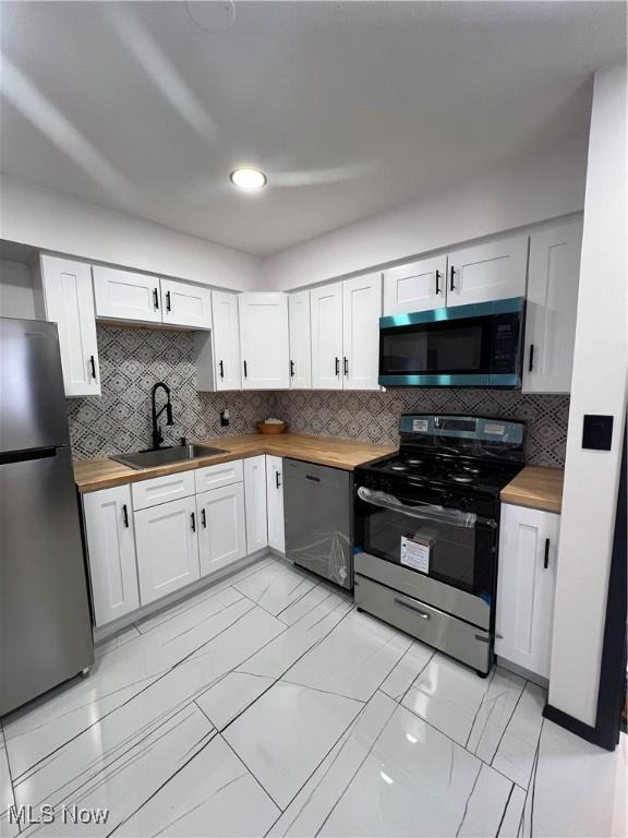 kitchen with appliances with stainless steel finishes, wooden counters, sink, and white cabinetry