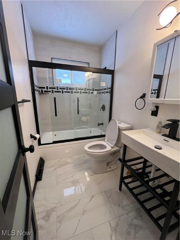 bathroom featuring toilet and shower / bath combination with glass door