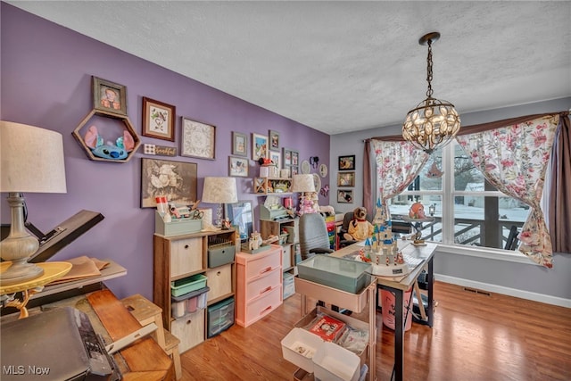 office space featuring an inviting chandelier, a textured ceiling, and light hardwood / wood-style flooring