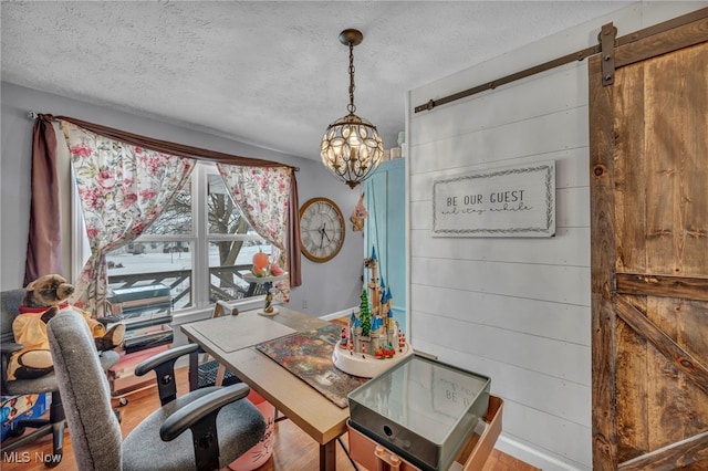 home office featuring a barn door, wood walls, wood-type flooring, a textured ceiling, and an inviting chandelier