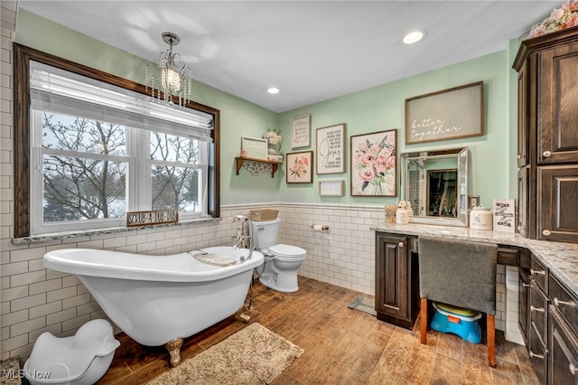 bathroom featuring a bath, tile walls, vanity, and toilet