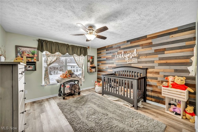 bedroom with ceiling fan, light wood-type flooring, wooden walls, and a nursery area