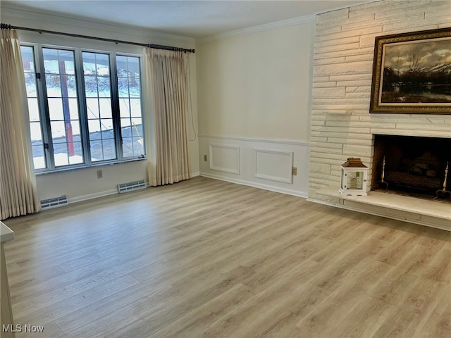 unfurnished living room with ornamental molding, light hardwood / wood-style flooring, and a stone fireplace