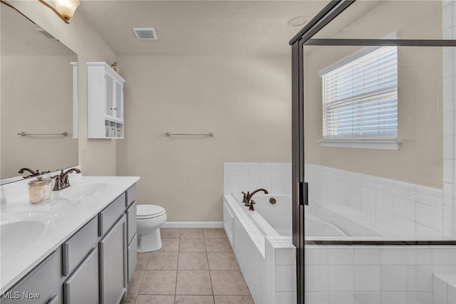 bathroom with tile patterned flooring, vanity, tiled bath, a textured ceiling, and toilet