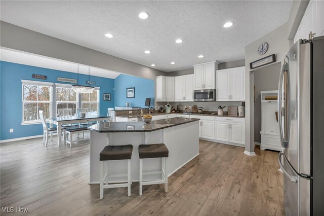 kitchen with pendant lighting, appliances with stainless steel finishes, a textured ceiling, a kitchen island, and white cabinetry