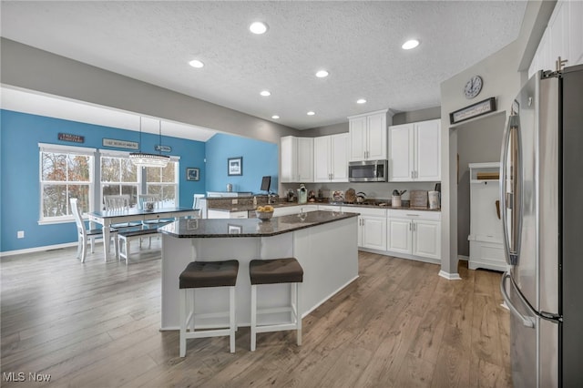 kitchen featuring a kitchen island, appliances with stainless steel finishes, white cabinets, hanging light fixtures, and a textured ceiling