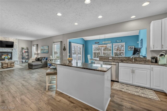 kitchen featuring a textured ceiling, stainless steel dishwasher, white cabinets, and hanging light fixtures