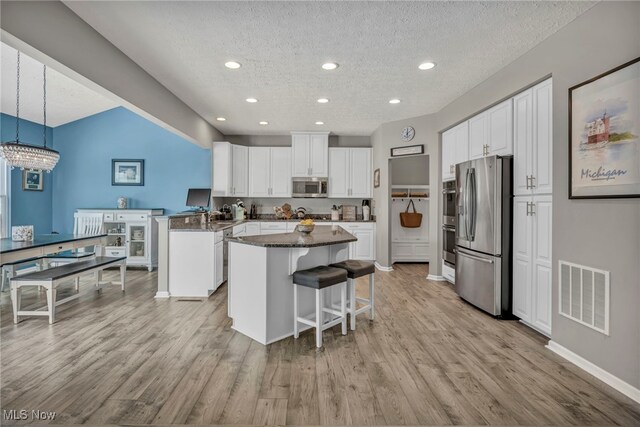 kitchen featuring kitchen peninsula, appliances with stainless steel finishes, pendant lighting, white cabinets, and a breakfast bar