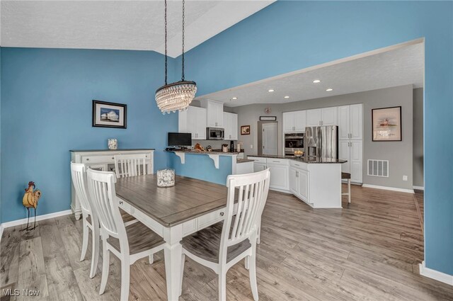 dining room with vaulted ceiling, a textured ceiling, a chandelier, and light hardwood / wood-style flooring