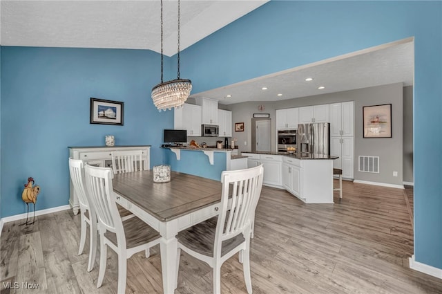 dining room with an inviting chandelier, vaulted ceiling, light hardwood / wood-style floors, and a textured ceiling