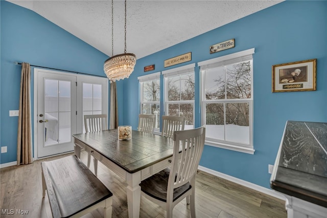 dining space with hardwood / wood-style flooring, vaulted ceiling, a textured ceiling, and a notable chandelier