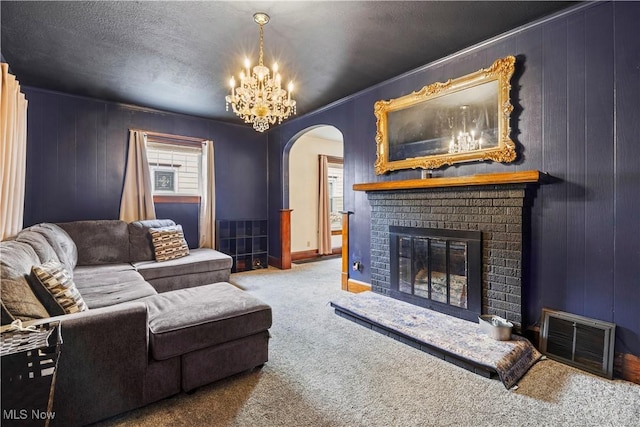 carpeted living room with a brick fireplace, a textured ceiling, wood walls, and a chandelier