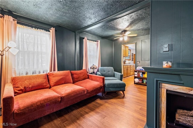 living room featuring hardwood / wood-style floors, beamed ceiling, ceiling fan, a fireplace, and a textured ceiling