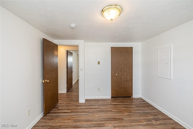 unfurnished bedroom with electric panel, a textured ceiling, a closet, and dark hardwood / wood-style flooring