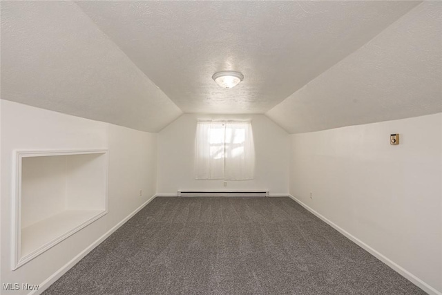 additional living space featuring a baseboard heating unit, a textured ceiling, dark colored carpet, and vaulted ceiling