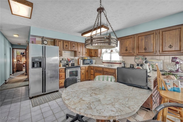 kitchen featuring decorative light fixtures, a textured ceiling, appliances with stainless steel finishes, and light tile patterned floors