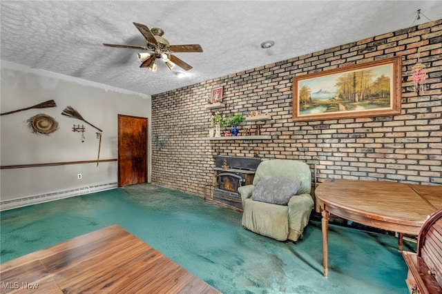 unfurnished room featuring a textured ceiling, a wood stove, ceiling fan, brick wall, and baseboard heating