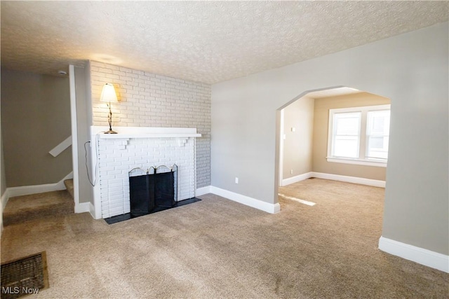 unfurnished living room with a textured ceiling, a brick fireplace, and carpet