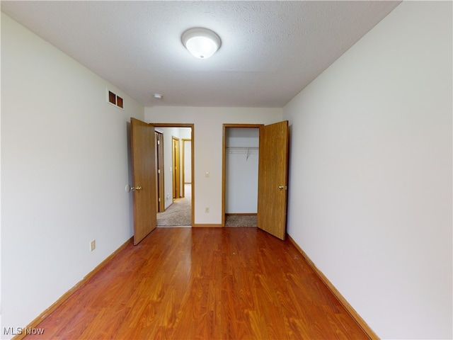 unfurnished bedroom featuring wood-type flooring, a closet, a textured ceiling, and a spacious closet