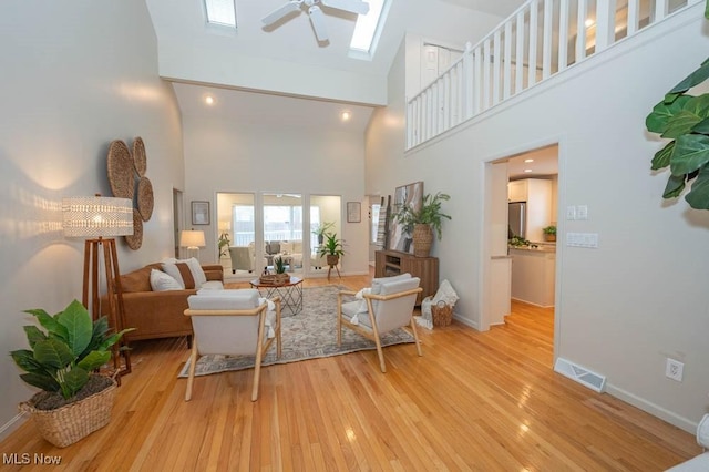 living room featuring a skylight, a towering ceiling, ceiling fan, and light hardwood / wood-style flooring