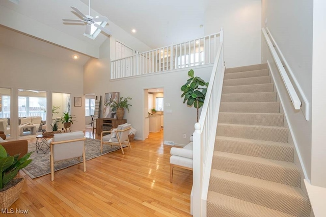 staircase featuring hardwood / wood-style floors, high vaulted ceiling, and ceiling fan