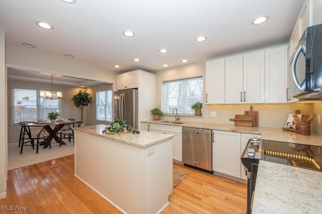 kitchen featuring sink, decorative light fixtures, white cabinets, light stone countertops, and appliances with stainless steel finishes