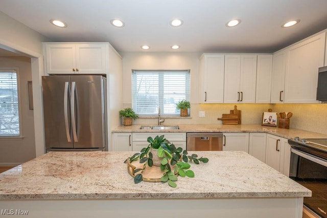 kitchen featuring white cabinets, stainless steel appliances, light stone counters, decorative backsplash, and sink