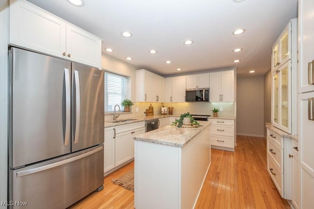 kitchen with stainless steel appliances, sink, white cabinets, a center island, and light wood-type flooring